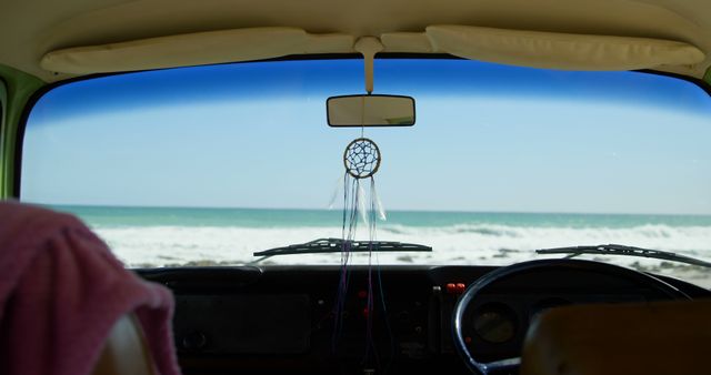 Shot from inside van on beach with dreamcatcher hanging from mirror, suitable for travel blogs, beach vacation promotions, road trip lifestyle content.