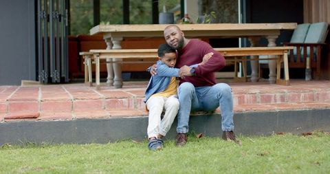 African american father hugging son on patio steps showing wristwatch, intimate family bond
