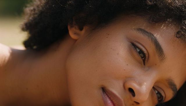 Sunlit black woman resting, tilting head and gazing sideways closeup portrait with curly hair
