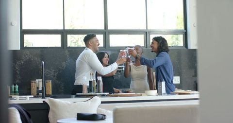 African american friends celebrating and toasting with wine at modern kitchen island