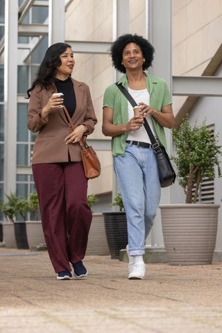 Diverse coworkers walking with coffee outside modern urban office building on casual workday