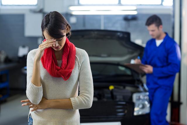 Worried customer standing while mechanic examining car in background at repair garage