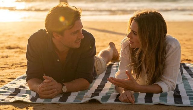 Couple lying on striped beach blanket chatting at sunset golden hour romance