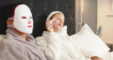 Couple enjoying at-home spa night with led facial mask and handheld skincare device