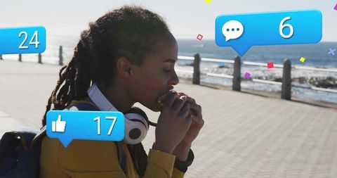 Young Woman Enjoying Sandwich by Seaside Walkway with Social Media Icons