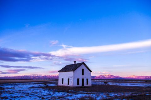 Old White House Standing on Snowy Plain at Twilight with Purple Mountain Sunset Glow