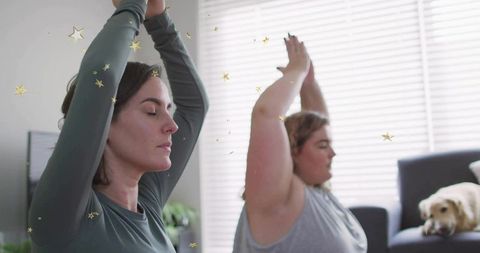 Women practicing yoga poses with pet in tranquil living room