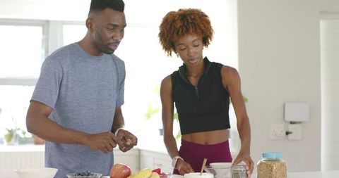 Black couple chopping and arranging fruit on white kitchen island for healthy breakfast