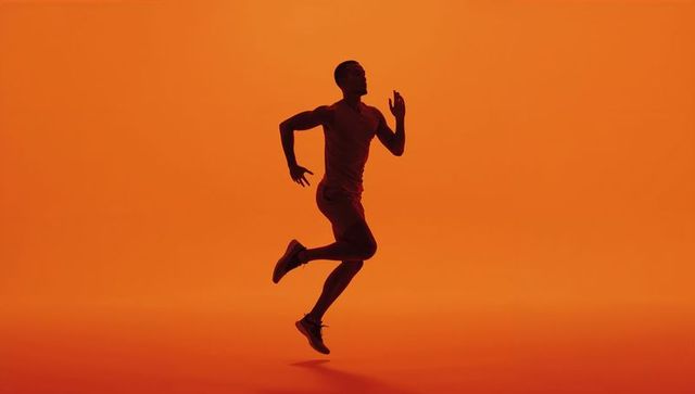 Silhouette of Male Athlete Running Against Orange Background
