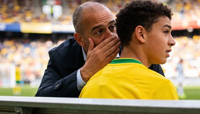 Coach whispering strategic instructions to young football player on sideline bench