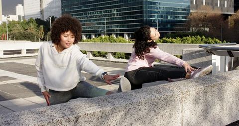 Urban rooftop friends stretching on concrete wall showing smartwatch for fitness lifestyle