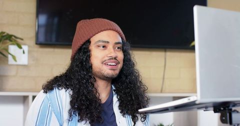 Young man wearing beanie working at laptop in modern home workspace, remote productivity