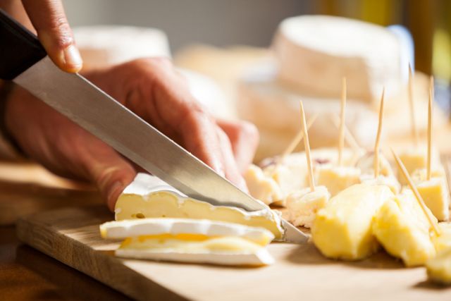Hand of staff cutting cheese at counter in market