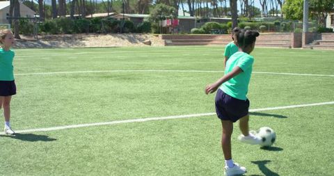 Girls kicking soccer ball on sunny school field during youth team practice session
