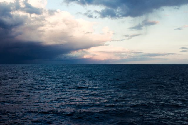 This image captures a dramatic seascape with dark storm clouds approaching over the ocean during evening. The contrast between the dark clouds and the calmer portion of the sky adds a sense of tension and dramatic effect. Ideal for use in articles about weather, natural phenomena, travel, adventure, and mood settings in both creative and commercial projects.