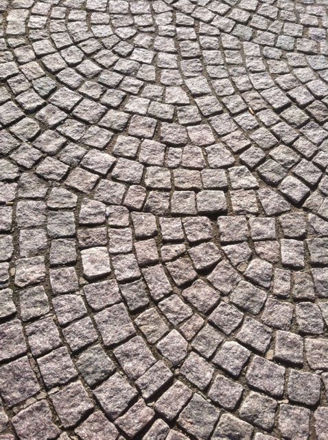Close-up view of a cobblestone path with an intricate circular pattern. The stones are gray with natural textures and create a visually pleasing design. Ideal for use as a background, in architectural concepts, design projects, outdoor space planning, or cityscape themes.