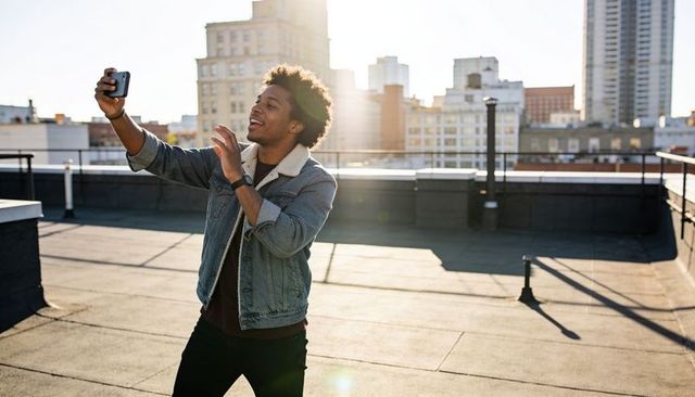 Urban rooftop vlogger taking selfie during golden hour wearing denim jacket and wristwatch