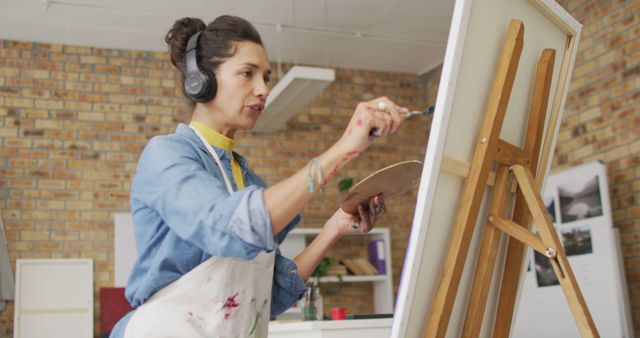 Image of biracial female artist in headphones painting in studio. Art, crafts, creativity and creation process concept.