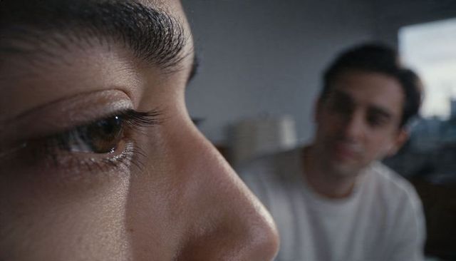 Intimate close-up of woman eye and profile with partner blurred in window light, emotional portrait