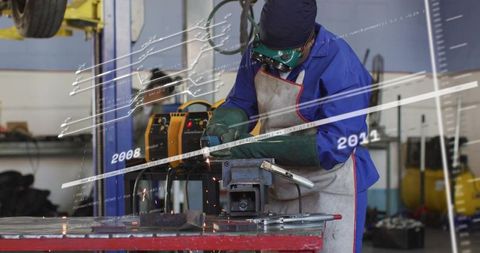 Welder Wearing Protective Gear Welding Metal with Sparking Torch at Industrial Workbench