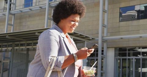 Joyful Woman Checking Phone While Walking in Urban Environment