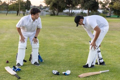 Young teammates adjusting cricket pads on dusk-lit ground preparing for training