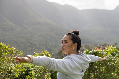 Asian woman stretching arms on misty mountain panorama for wellness and outdoor fitness