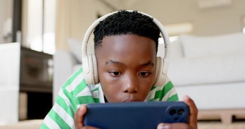 African american boy playing mobile game on smartphone while wearing white headphones