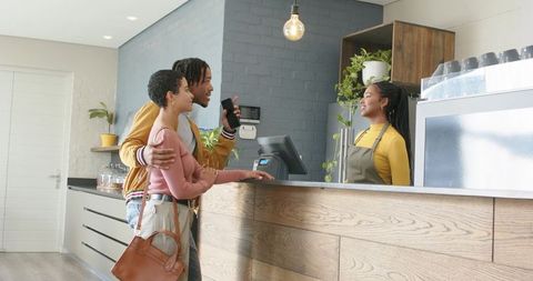 Young couple chatting with african american barista while ordering coffee at modern cafe