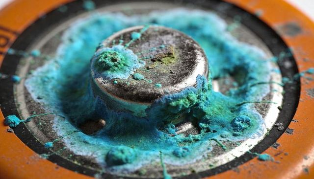 Corroded battery terminal showing turquoise and green oxidation nodules on orange casing