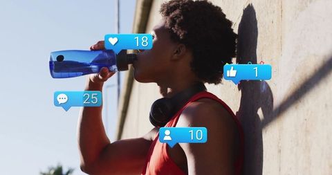 Urban athlete hydrating after workout with blue bottle, headphones, social notifications