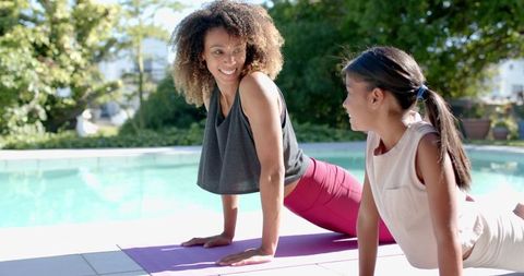 Mother and Daughter Practicing Yoga Outside by Pool on Sunny Day