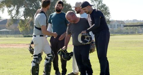 Baseball teammates standing on infield wearing catcher's gear and holding helmets, teamwork