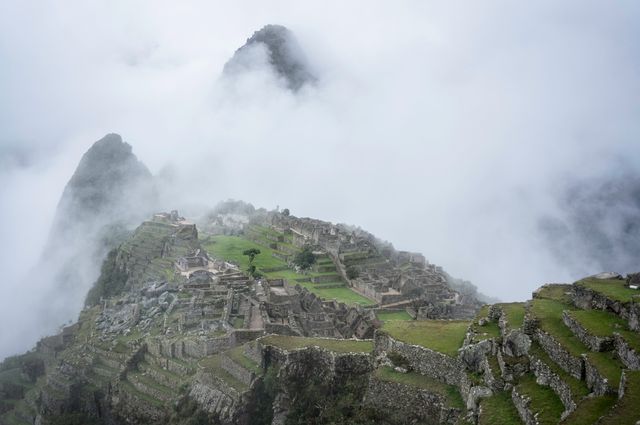 Machu Picchu surrounded by mist, historic Inca site nestled in Andes Mountains. Ideal for travel blogs, history sites, cultural content, portraying adventure, and promoting tourism in Peru.