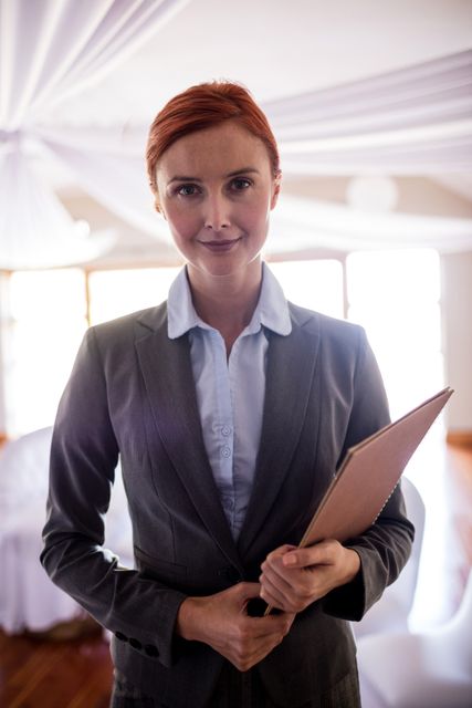 Beautiful female manager standing with file in hotel