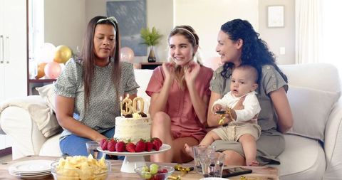 Women and a young child enjoying a 30th birthday celebration at home with a beautifully decorated cake. Ideal for use in family celebration materials, birthday party invitations, and marketing content focused on friendship and family joy. The casual setting enhances a warm and personal vibe, perfect for seasonal greetings or lifestyle blogs centered on common experiences and life milestones.