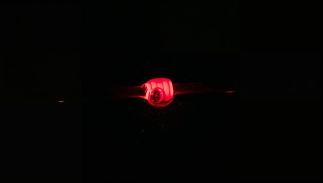 Molten glass bead melting on rod emitting red glow and sparks