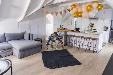 African american man laying rug in bright loft living room with party decorations