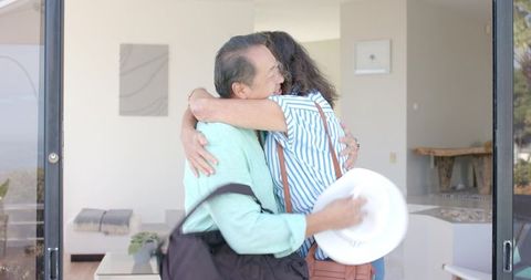 Senior friends hugging at glass doorway, embracing connection indoors