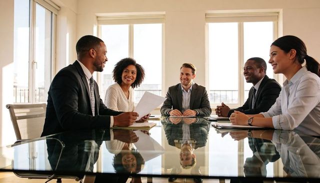 Multicultural business team collaborating at glass conference table during daytime meeting