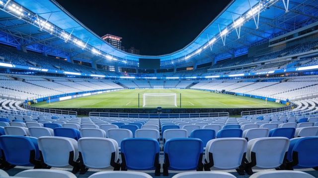 Empty modern soccer stadium glowing under floodlights with blue and white seating