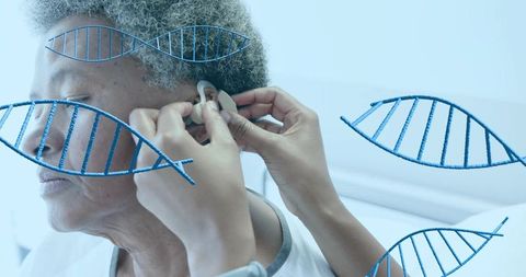Caregiver fitting hearing aid on senior patient with dna helix overlays for genetics
