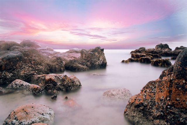 Image captures a serene seascape with rocky shoreline at sunset. Ideal for projects related to nature, travel, tranquility, and relaxation. Use in promotional materials for beach resorts, greeting cards, desktop wallpapers, or inspirational posters.