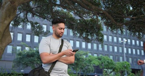 African american commuter using smartphone under tree near office building