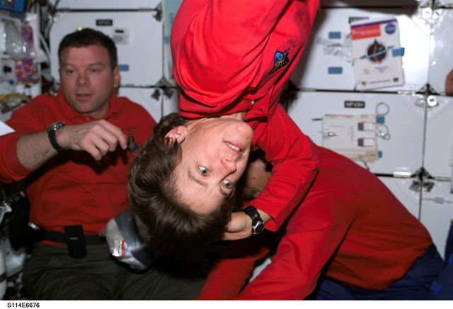 Astronaut Wendy B. Lawrence is floating freely inside the middeck of the Space Shuttle Discovery during the STS-114 mission while docked to the International Space Station. Astronauts James M. Kelly and Charles J. Camarda are in the background. This can be used to emphasize teamwork, space exploration, life in space, or NASA missions.