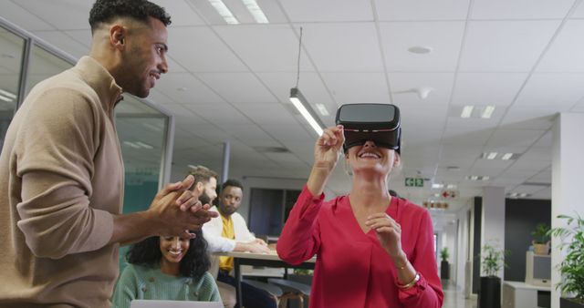 Colleagues in a modern office enjoying virtual reality technology. One person is wearing a VR headset while others observe and laugh. This vibrant image reflects teamwork, technological advancement, and a fun workplace environment. Perfect for use in articles and presentations relating to modern office culture, teamwork, and new technologies.