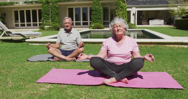 Happy caucasian senior couple practicing yoga meditating in garden in the sun. at home in isolation during quarantine lockdown.