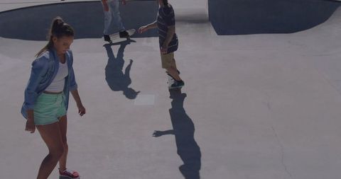 Teen skaters rolling through concrete bowl, sunlit shadows and casual summer streetwear