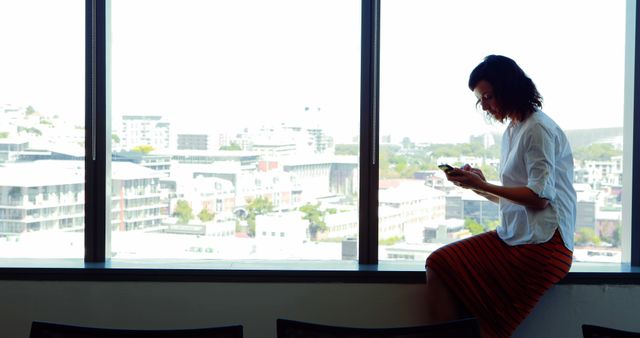 Female executive using mobile phone near the window in office