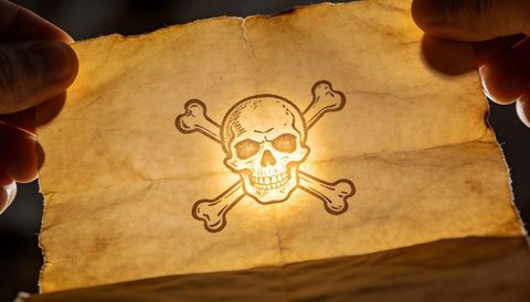 Holding aged parchment backlit by warm glow featuring skull-and-crossbones on vellum paper
